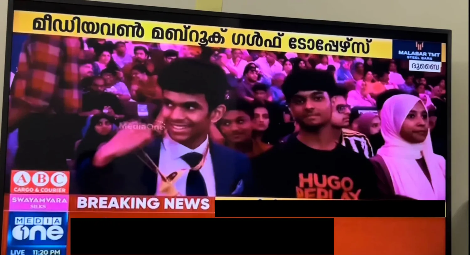 A TV showing MediaOne’s Mabrook Gulf Toppers broadcast, Dubai: me in a suit wearing the medal, among other students in the audience